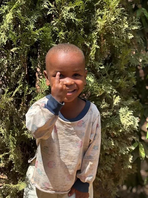 A smiling child giving a thumbs-up beside greenery
