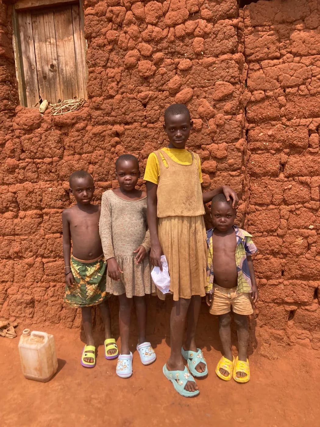 Four children standing beside the earthen wall of their home